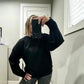 woman wearing a black crew neck sweatshirt, taking a selfie in front of a mirror